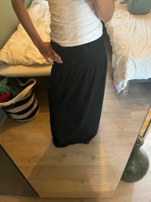 Svart långkjol i bomull - En svart långkjol med enkel och rak passform. Kjolen är tillverkad i mjukt bomullstyg och har en hög midja som ger en snygg siluett. Perfekt att styla med en enkel topp eller stickad tröja.