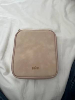 Braun epilator med tillbehör i väska - Säljer en Braun epilator i en ljusbeige, fyrkantig väska med dragkedja. Setet innehåller flera utbytbara huvuden och laddare,Perfekt för smidig hårborttagning hemma. Nypris-2700kr