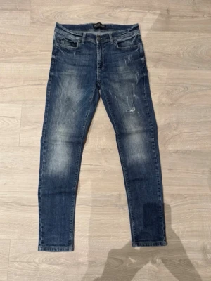 Blå slitna skinny jeans - Säljer ett par blå skinny jeans med slitningar och lätt tvättade detaljer. Jeansen har fem fickor, dragkedjegylf och smal passform. Perfekta för en avslappnad och trendig look.