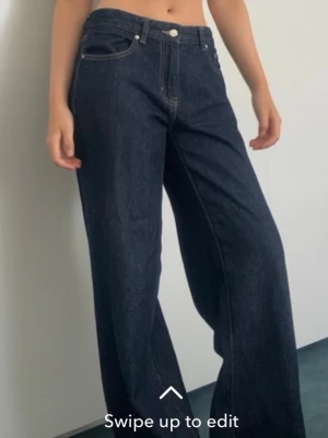 Mörkblåa wide leg jeans - Säljer ett par mörkblåa jeans med wide leg passform och midwaist midja. Jeansen har klassiska fem fickor och kontrastsömmar. Perfekta för en avslappnad och trendig look. Materialet är kraftig denim i bomull. Har sytt in de vid midjan så de sitter bättre. 