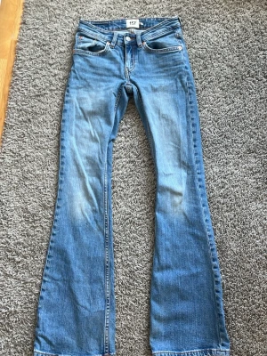 Blå bootcut jeans med utsvängda ben - Säljer ett par ljusblå bootcut jeans med utsvängda ben och klassiska fem fickor. Jeansen har en snygg tvätt och detaljerade sömmar. Perfekta för dig som gillar retrostil och vill ha ett par jeans som sticker ut lite extra.