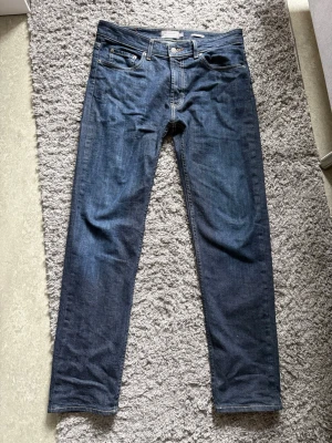 Mörkblå raka jeans Dressmann - Snygga mörkblå jeans med rak passform och klassisk femficksdesign. Jeansen har kontrastsömmar och bälteshällor. Perfekta för en stilren och enkel look. Materialet är denim i bomull.