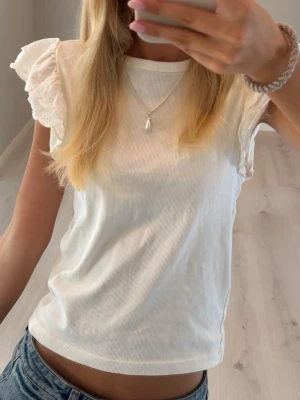 Vit topp med volangärmar - Supersöt vit topp med volangärmar i spets och rund halsringning. T-shirten är ärmlös med romantiska detaljer och passar perfekt till jeans eller kjol. Materialet känns mjukt och lätt, perfekt för varmare dagar. Sitter som en xs💕💕