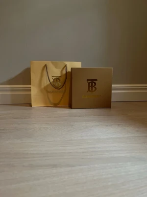 Burberry randigt bälte med silverdetalj - Säljer ett Burberry bälte med klassiskt randigt mönster i beige, svart och vitt. Bältet har ett stort silverfärgat spänne med Burberrys logotyp. Kommer med originalförpackning och dustbag.