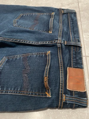  Nudie jeans - Snygga mörkblå jeans från nudie jeans med klassisk rak passform och fem fickor. Jeansen har kontrastsömmar och subtila detaljer på bakfickorna. Perfekta för dig som gillar en tidlös och stilren look. W29 L32