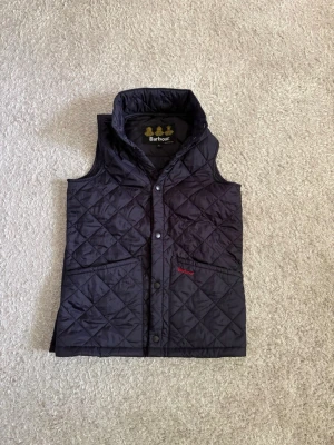 Barbour quiltad väst - L barn/ca XS/S vuxen - Marinblå quiltad väst från Barbour i storlek L barn. Kan ungefär motsvara XS/S i vuxenstorlek beroende på önskad passform. Sparsamt använd och i mycket bra skick utan tydligt slitage.  Klassisk quiltad modell med fickor framtill och broderad Barbour-logga.  📦 Snabb leverans! 💬 Hör gärna av dig vid frågor eller om du vill ha fler bilder/mått!