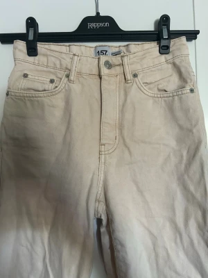 Beige raka jeans med hög midja - Säljer ett par beige jeans med hög midja och raka ben. Klassisk femficksmodell med knapp- och dragkedjestängning. Jeansen har en avslappnad passform och är tillverkade i ett kraftigare denimtyg. Perfekta för en stilren och enkel look.