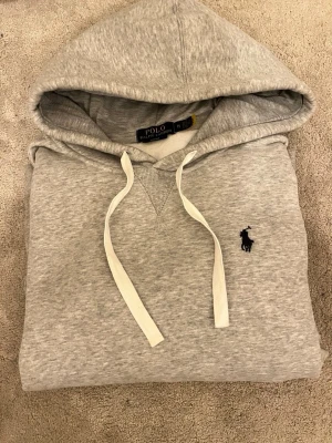 Grå hoodie från Polo Ralph Lauren - Snygg grå hoodie från Polo Ralph Lauren i slim fit-modell. Klassisk design med huva, vita dragsnören och broderad logga på bröstet. Tillverkad i mjukt material som känns skönt mot huden. Perfekt för en avslappnad och stilren look.Priset går att diskutera vid snabb affär, finn de frågor så är de bara o skriv 😊