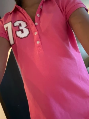Rosa vintage L.BRADOR polo - ÄKTA L.BRADOR från tidigt 2000-tal 🩷 Hot pink piqué polo med "73" varsity print på ärmen. Knappar med logga/print. Tight baby tee passform. Perfekt till låga jeans + klackar. RARE färg + märke. Y2K mall girl, coquette, sporty babe aesthetic.