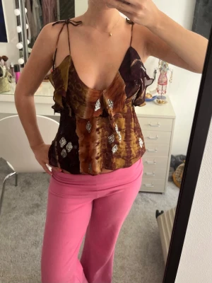 Brun linnetopp med paljetter från Zara  - Säljer en unik linnetopp med tunna axelband och djup urringning. Volangdetaljer framtill och silver paljetter. Från Zara och endast använd en gång, säljs ej längre 
