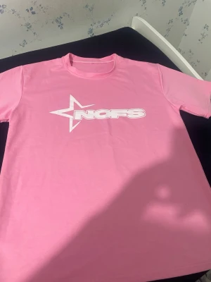 Rosa set med t-shirt och shorts - Säljer ett rosa set med matchande t-shirt och shorts. Båda plaggen har ett vitt tryck med stjärna och texten 'NOFS' framtill. T-shirten har rund hals och korta ärmar, shortsen har resår och dragsko i midjan. Mjukt och bekvämt material, perfekt för avslappnade dagar.Vi kan komma överens med priset