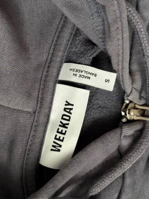 Grå hoodie med dragkedja från Weekday - Grå hoodie från Weekday i storlek S. Modellen har dragkedja framtill, huva med dragsko och två fickor. Tillverkad i mjukt material som känns skönt mot huden. Perfekt för en chill och avslappnad stil.