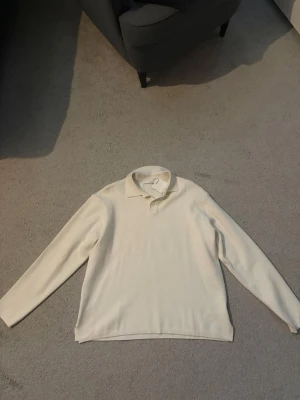 Klassisk vit långärmad pikétröja - En stilren vit långärmad pikétröja med krage och knappar vid halsen. Tröjan har en rak passform och är tillverkad i ett mjukt material som känns skönt mot huden. Perfekt för en clean och enkel look.