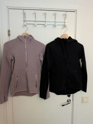 Träningströjor med dragkedja - Säljer två snygga träningströjor med dragkedja och luva. Den dimlila är stretchig och är från H&M Sport i storlek XS. Den svarta är ett styvare lite tjockare material från SOC i storlek XS. Köp en för 50 kr eller båda för 70 kr.