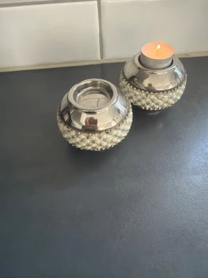 Silvriga ljushållare med pärldekor - Två runda ljushållare i silverfärgat metall med dekorativa pärlor runt om. Passar perfekt för värmeljus och ger ett elegant intryck till rummet. Säljes som par och har en glansig yta med pärlstruktur.