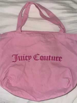 Rosa shoppingväska från Juicy Couture - Säljer en stor och rymlig rosa shoppingväska från Juicy Couture. Väskan är i mjukt tyg med två handtag och har Juicy Couture-broderi i rosa framtill. Perfekt för att bära med sig allt man behöver till skolan eller stan.