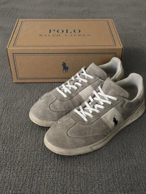 Polo Ralph Lauren HRT AERA Sneakers Beige/Grå – EU 43 – Originalkartong - Säljer ett par Polo Ralph Lauren HRT AERA sneakers i en stilren beige/grå färg. Skorna är i bra använt skick med normala tecken på användning, främst på sulorna och vissa partier av ovandelen (se bilder).  * Storlek: EU 43 (US 10) * Modell: HRT AERA PP-SK-LTL * Material: 100% läder * Foder: 100% textil * Yttersula: 100% gummi * Färg: Beige/Grå * Originalkartong ingår.  Perfekta som vardagsskor och lätta att matcha med både jeans och chinos.  📦 Skick  Bra  🏷️ Varumärke  Polo Ralph Lauren