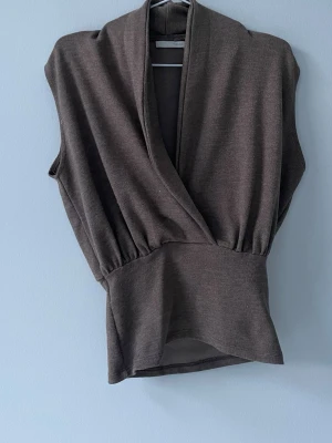 Brun omlottopp från Zara - Säljer en brun omlottopp från Zara i mjukt material. Toppen är ärmlös med bred midjeresår och har en djup v-ringning framtill. Perfekt att styla med jeans eller kjol för en trendig look.