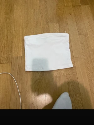 Vit bandeau tubtopp från H&M Divided - Säljer en enkel och stilren vit bandeau tubtopp från H&M Divided. Toppen är ribbad och ärmlös, perfekt för sommardagar eller som layering-piece. Passformen är tight och materialet är mjukt och stretchigt för extra komfort.