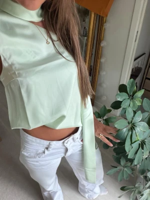 Ljusgrön satinlinne med scarfdetalj - Trendig ljusgrön topp i satin med lös passform och unik scarfdetalj runt halsen. Ärmlös design och croppad längd som ger en modern look. 