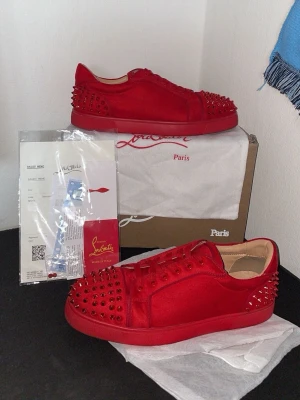 Sällsynta röda  Louboutin skor - Snygga röda sneakers från Christian Louboutin med matchande röda nitar över hela skon. Tillverkade i mocka och läder med klassisk röd sula och lågt skaft. Perfekta för dig som vill sticka ut med en exklusiv och edgy stil. I riktigt fint skick fast de är använda🫡 Frågor? Bara att skriva🙌