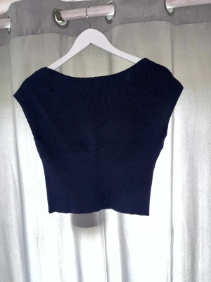 Svart ribbad croppad topp - Snygg svart croppad topp med v-ringning och ribbad struktur. Toppen är ärmlös och har en tight passform som framhäver figuren. Perfekt att matcha med höga jeans eller kjol för en trendig look.