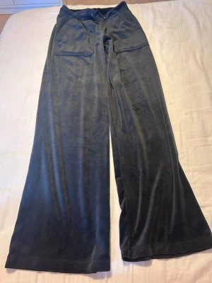 Svarta vida mjukisbyxor i velour - Säljer ett par svarta mjukisbyxor i mjuk velour med breda ben och dragsko i midjan. Byxorna har fickor på sidorna och en avslappnad passform som är perfekt för chill dagar. Supersköna och trendiga för dig som gillar comfy stil.