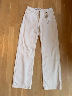 Vita raka jeans midwaist - Säljer ett par helt nya vita jeans från BikBok med rak passform och hög midja. Jeansen har klassiska fem fickor och bälteshällor. Materialet är kraftigt denim i bomull och de har en enkel, clean look som passar till allt.   Storlek 26/32