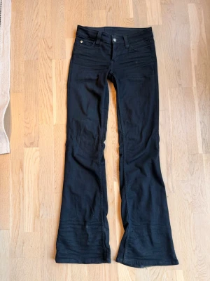 Svarta bootcut jeans weekday - Snygga svarta jeans med bootcut-modell och låg midja. Klassisk femficksdesign och knappgylf. Jeansen har en cool patch bak i midjan och är perfekta för dig som gillar en retro vibe. Materialet är stretchigt för extra komfort.