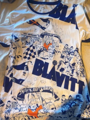 IFK Göteborg Blåvitt t-shirt LIMITED - Säljer en vit t-shirt med blått och orange tryck från IFK Göteborg. T-shirten har korta ärmar och ett stort BLÅVITT-tryck samt illustrationer av supportrar och flaggor. Perfekt för dig som älskar fotboll och vill visa ditt stöd för laget. Limited, finns inte och köpa någon annanstans vad jag vet. Storlek M men passar S