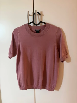 Rosa stickad t-shirt  - Säljer en stickad t-shirt från LINDEX. Tröjan är rosa, har korta ärmar, rund halsringning och ribbade kanter. Bekväm men inte så använd, då den är lite liten