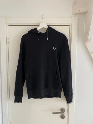 Fred Perry hoodie - Svart hoodie från Fred Perry med vit logga på bröstet. Hoodien har luva. Väldigt bra skick.