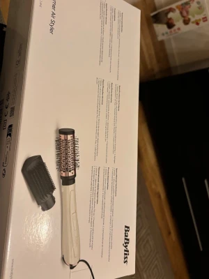 BaByliss Shimmer Air Styler borste - Volymborste från BaByliss i beige och roséguld med rundad form och borsthuvud i metall. Inkluderar ett extra borsttillbehör i svart plast. Perfekt för att styla och skapa volym i håret med smidig hantering.