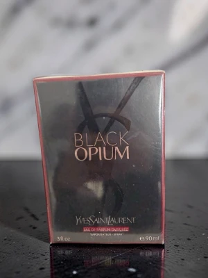 Parfym Yves Saint Laurent Black Opium  -  Parfym Black Opium från Yves Saint Laurent är en ikonisk parfym i en elegant svart och roséguldig förpackning. Flaskan rymmer 90 ml och har en lyxig design med metalliska detaljer och tydlig logotyp. Doften är känd för sin djupa, sensuella karaktär.