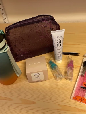 Skönhetskit med necessär och tillbehör - Ett komplett skönhetskit med en lila meshnecessär med blommönster från The Body Shop, ansiktsrengöring från aila, risbaserad ansiktskräm, två små sprayflaskor, pincett och sminkborstar. Perfekt för dig som gillar att ta hand om huden och vill ha allt samlat.