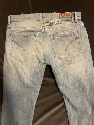 Dondup jeans  - Säljer ett par ljusblå jeans med slitningar och hål på både fram- och baksida. Jeansen har fem fickor och en klassisk knappgylf. Materialet är denim och passformen är rak med en något smal siluett. Perfekta för en avslappnad och trendig look.