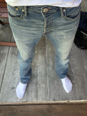 Blå slim straight jeans från Jack and Jones  - Säljer ett par klassiska blå jeans från Nudie i modellen Slim Straight/Tim. Jeansen har en rak passform med smal siluett, fem fickor och snygga kontrastsömmar. Tillverkade i slitstark bomull med en tidlös tvätt.