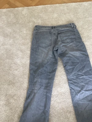 Gråa raka jeans - Säljer ett par gråa jeans med rak passform  Jeansen har bälteshällor och knappgylf. Materialet är denim i bomull och färgen är tvättad grå, perfekt för en avslappnad stil.