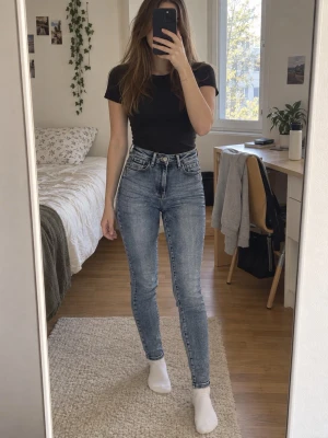 Blå high waist skinny jeans - Säljer ett par blå high waist skinny jeans med klassisk femficksdesign och dragkedja. Jeansen har en snygg tvättad look och smal passform som sitter tight hela vägen ner. Perfekta till en enkel t-shirt eller hoodie.