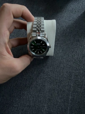 Silverfärgad klocka med länkarmband - Stilren klocka med silverfärgat länkarmband och svart urtavla. Klockan har markerade timindex och räfflad bezel som ger en klassisk look. Passar perfekt för dig som gillar tidlös design och metallarmband.