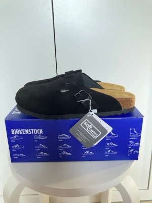  Birkenstock Boston sandaler - 41 - Stilrena svarta Birkenstock Boston sandaler i mocka med justerbart spänne och mjuk fotbädd. Klassisk slip-in modell med korksula och greppvänlig yttersula. Perfekta för dig som gillar bekväma och tidlösa skor. Storlek 41