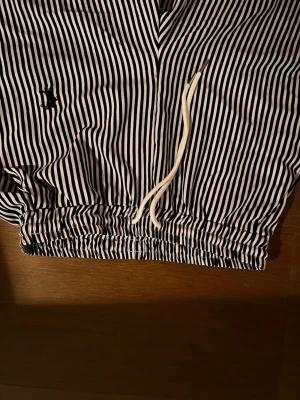 Randiga pyjamasbyxor med snörning - Snygga pyjamasbyxor med svarta och vita ränder samt resår och snörning i midjan. Byxorna har en liten broderad kanin på sidan och är perfekta för att chilla hemma. Mjukt och bekvämt material.