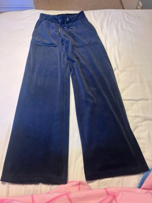 Mörkblå velour mjukisbyxor - Säljer ett par mörkblå mjukisbyxor i mjuk velour med breda ben och dragsko i midjan. Byxorna har stora fickor framtill och en avslappnad passform som är perfekt för chill dagar. Supersköna och trendiga för dig som gillar comfy vibes.