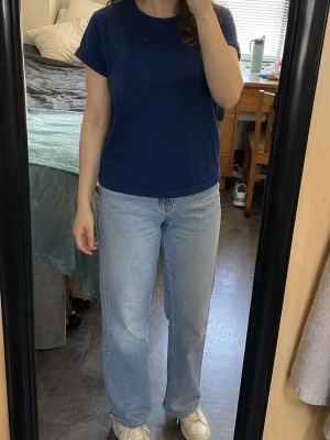 Mörkblå T-shirt / topp med uppvikta ärmar - Enkel och snygg mörkblå topp med rund halsringning och korta, uppvikta ärmar. Mjuk sweatshirtliknande trikå med ljusare insida. Rak och avslappnad passform – perfekt till jeans för en enkel vardagslook.  Storleksetiketten saknas, se bilder med mått för bästa passform.  Begagnat skick med normala tecken på användning. Se bilder. Box L
