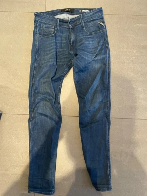 Replay anbass - Säljer ett par klassiska blå jeans från Replay med fem fickor och snygga kontrastsömmar. Jeansen har normal passform och är tillverkade i mjuk bomull med en liten mängd stretch för extra komfort. Perfekta till din vardagsstil!