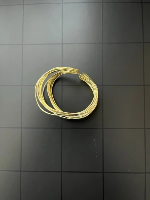 Guldfärgat statement-armband i spiraldesign - Snyggt guldfärgat statement-armband med modern spiral-/wire-design. Består av flera tunna metalltrådar som skapar en elegant, skulptural look runt handleden. Öppen modell som är enkel att ta på. Fint skick. Se bilder för passform, detaljer och mått.