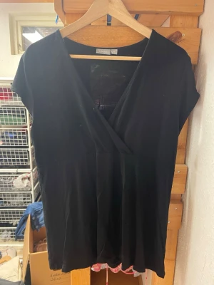 Svart omlottopp med v-ringning - En svart omlottopp med v-ringning och korta ärmar. Toppen har en enkel och stilren design som passar till många olika outfits. Tillverkad i mjukt tyg som känns skönt mot huden.
