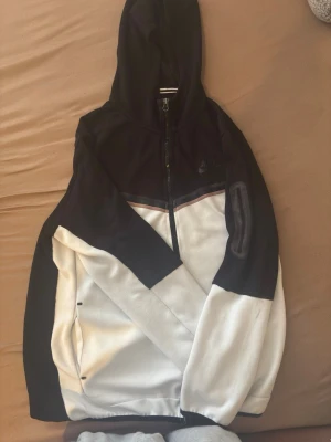 Svartvit hoodie från Nike - Snygg svartvit hoodie från Nike med dragkedja framtill och huva. Hoodien har en cool färgblock-design med svarta och vita partier samt diskreta detaljer. Perfekt för dig som gillar sportig och avslappnad stil.