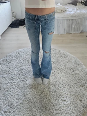 Ljusblå bootcut jeans med slitningar - Säljer ett par ljusblå bootcut jeans från Gina tricot 14+ med slitna detaljer och fickor fram. Jeansen har låg midja.