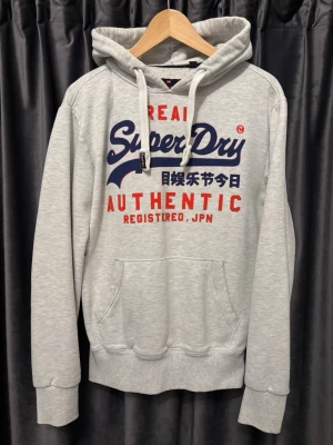 Superdry Hoodie - Superdry Hoodie - skick 8/10, jättefint skick förutom hålet (sista bilderna) - storlek S - sjukt snygg hoodie och väldigt bekväm att ha på sig - hålet kan lätt lagas för den som kan och vill - pris kan diskuteras - hör av er vid frågor🙌